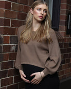 A woman in black and brown angel maternity 2 piece knitted cropped top and skirt set standing against the wall, side (6656401145959)